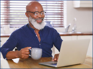Man holding a mug and looking at a laptop.