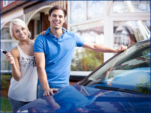 Couple holding keys while standing next to a car. 