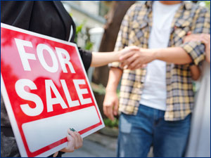 Man shaking hands with real estate agent standing by "For Sale" sign