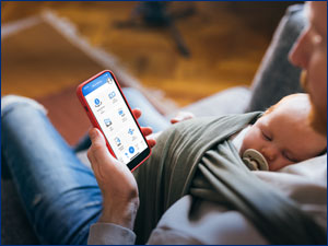man holding sleeping baby while looking at mobile phone