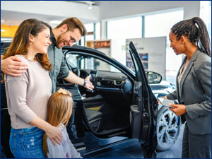 man woman and child with sales agent looking at a car