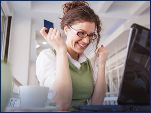 Woman celebrating while using computer and holding a credit card