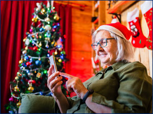 Woman using smartphone sitting next to Christmas tree
