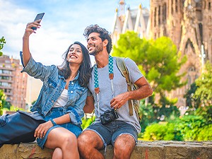 man and woman taking a selfie sitting on a ledge near a mountain
