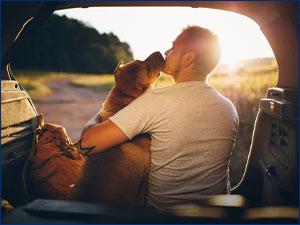 Man holding dog while sitting in the trunk of a car