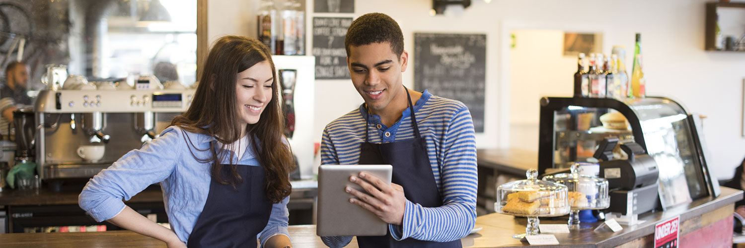 103-20-Youth-Accts-Web-Page-Hero-Final Two young coffee shop employees looking at a tablet