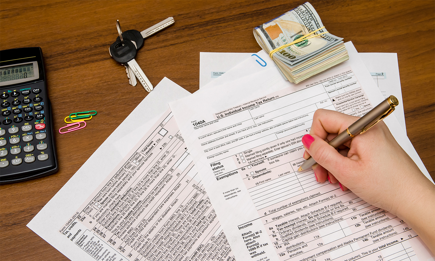 Car keys, cash and calculator on table while woman fills out tax documents