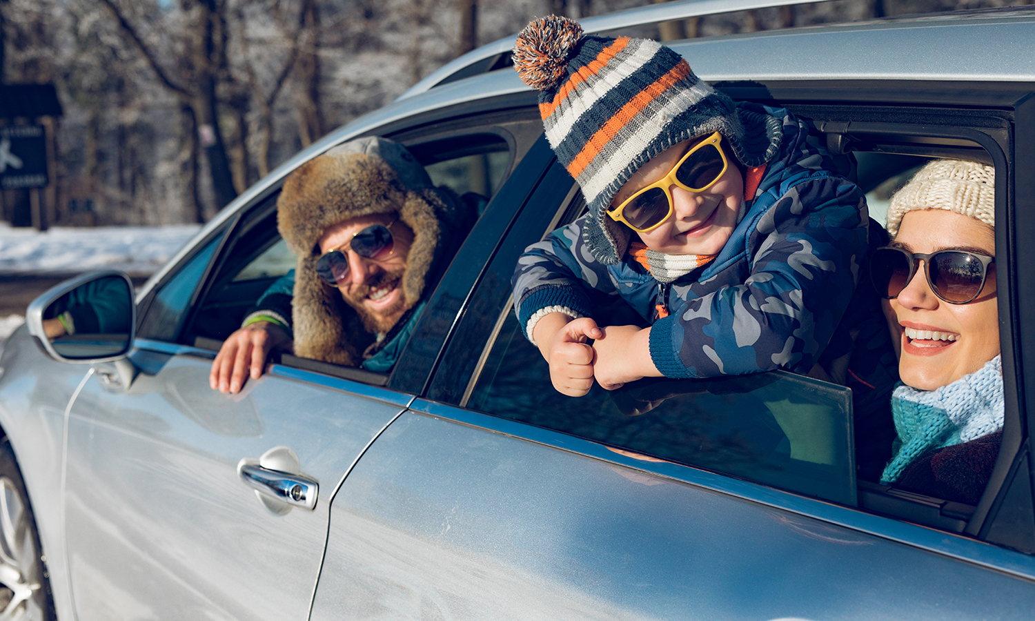 Family wearing winter clothes looking out car windows at snow