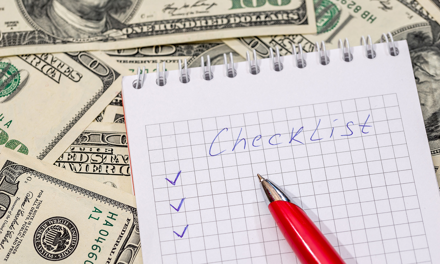 Hundred dollar bills under pad with checklist on it