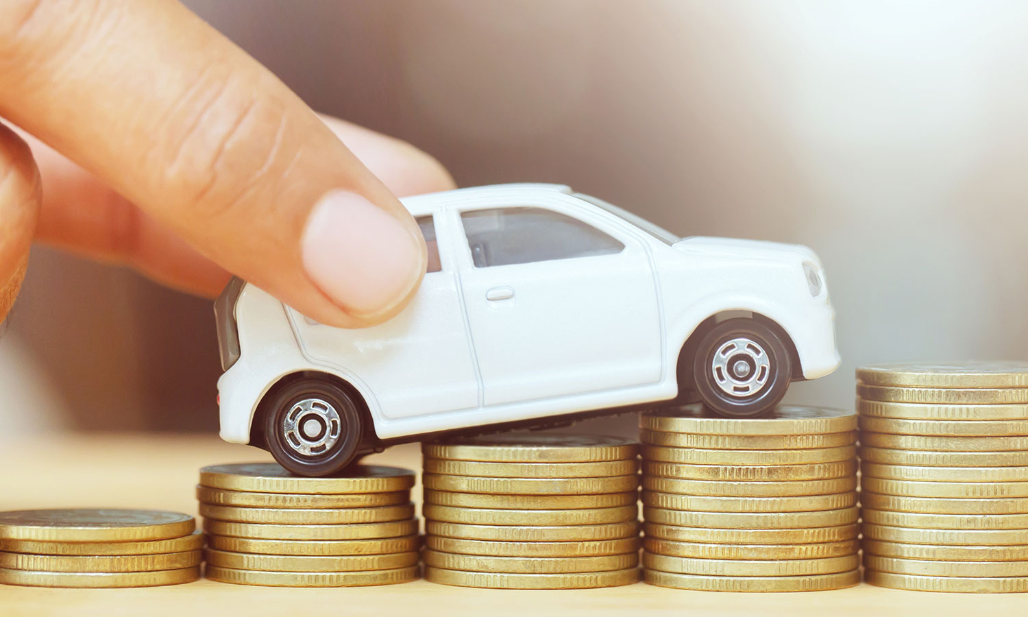 person holding toy car sitting on top of stacked pennies trending upward