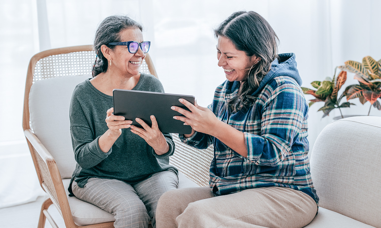 two women sitting in chairs reading a tablet