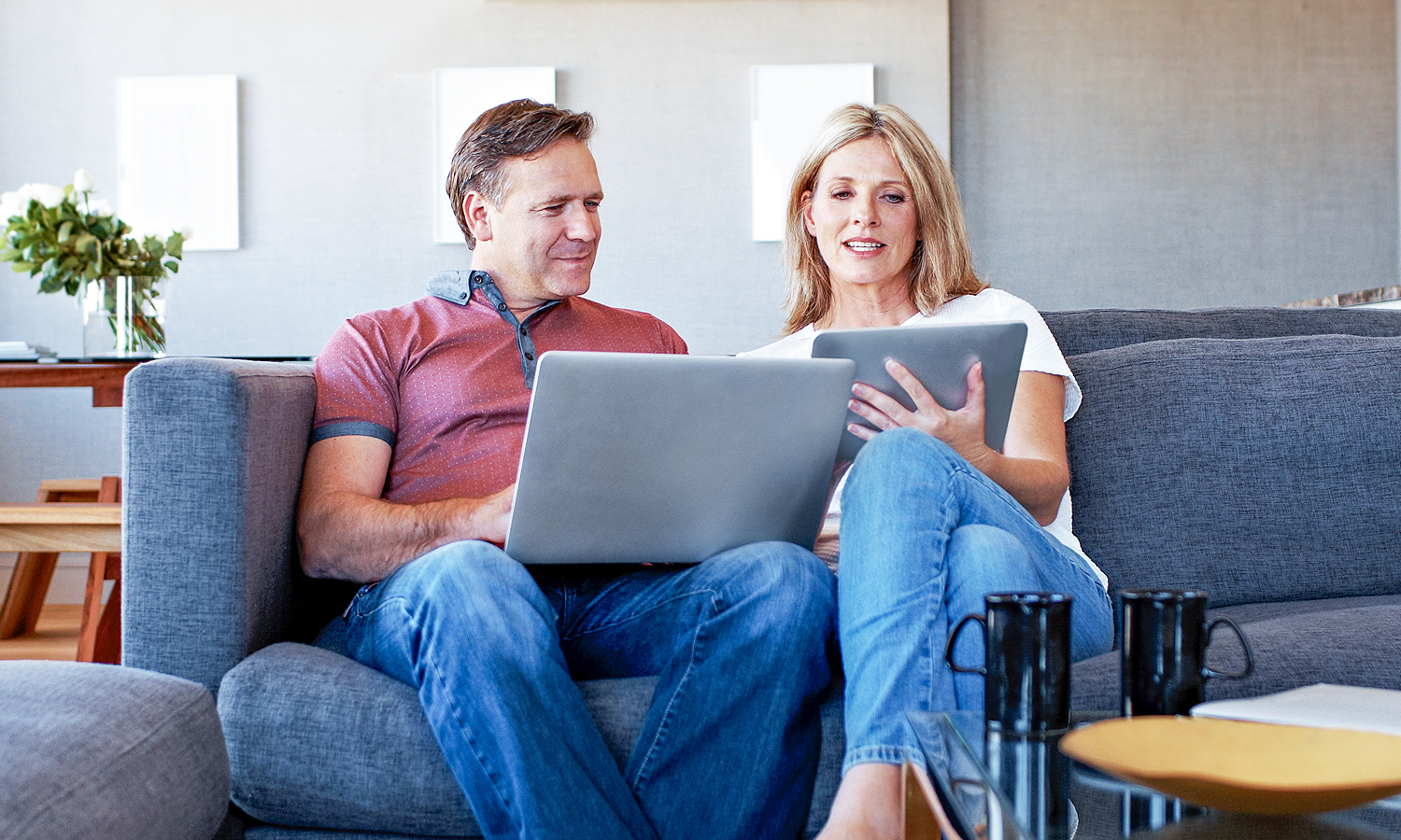 man and woman sitting on couch looking at tablet and laptop