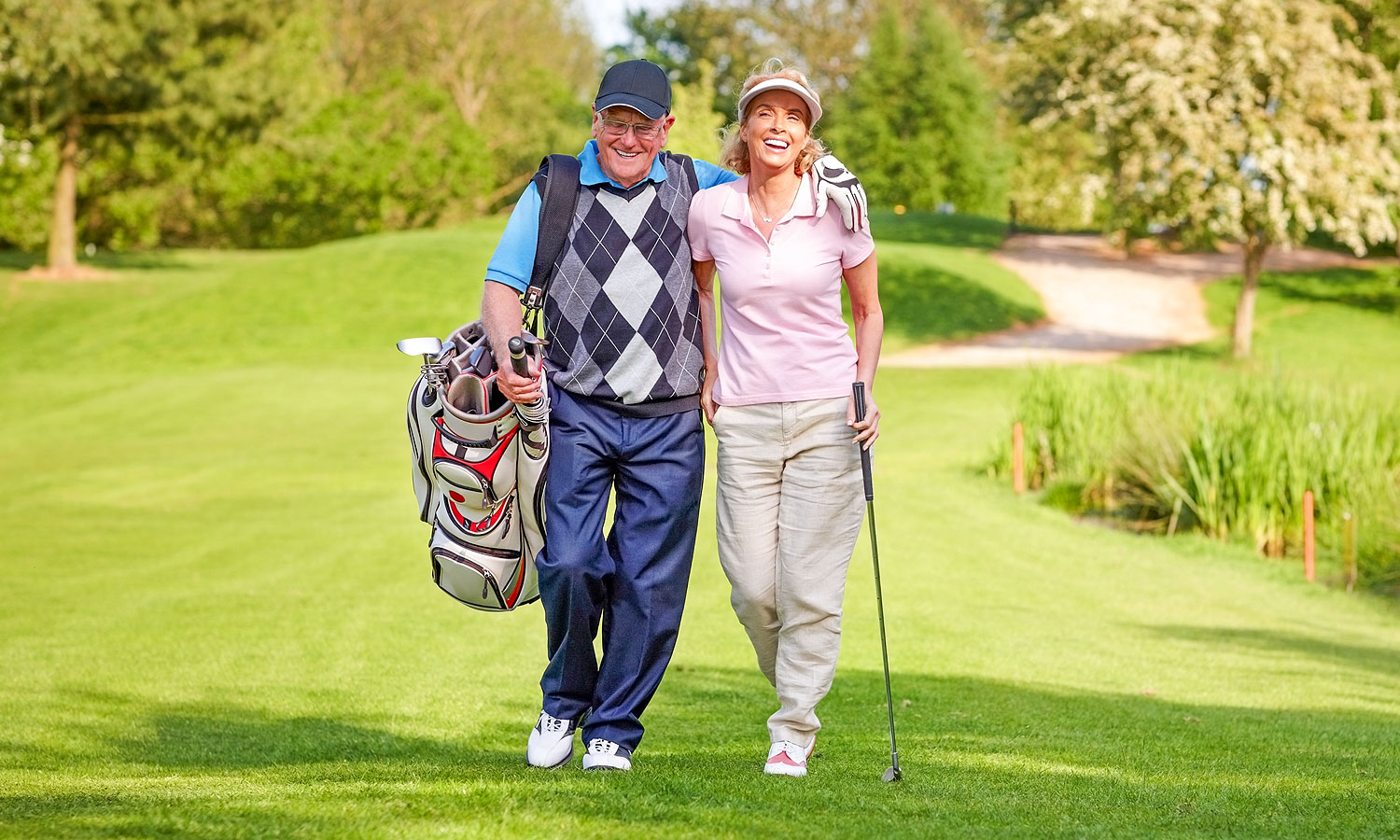 man and woman walking across a golf course while carrying a golf bag