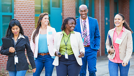 A group of five people wearing lanyards walking on the sidewalk